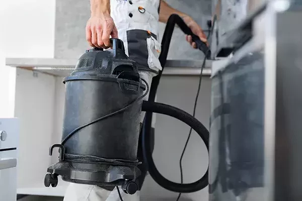 A cleaning technician carries a heavy-duty vacuum cleaner with hose attachment, preparing for deep cleaning in a post-construction environment.