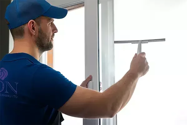 A cleaning technician in a blue uniform uses a squeegee to clean a glass window, ensuring a streak-free finish during post-construction cleaning.