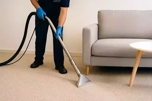 Cleaning specialist using a professional carpet extraction machine to deep clean a grey carpet in a living room, leaving a clearly defined clean path.