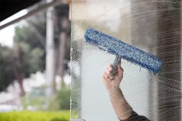 Hand holding a blue window cleaning tool scrubbing soapy water off a glass surface during exterior window cleaning.