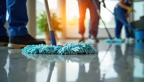 Close-up of a blue mop cleaning a shiny floor, with cleaning staff in the background mopping and maintaining the space.