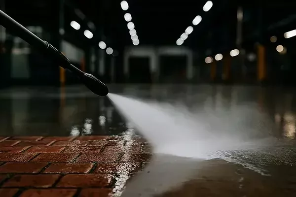High-pressure water jet cleaning an industrial concrete and brick floor, with a clear contrast between the cleaned and dirty sections.